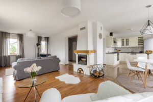Ein offen gestalteter Wohn- und Küchenbereich mit einem gemauerten Kamin, einem grauen Sofa und einem Essbereich mit weißem Tisch und Stühlen.