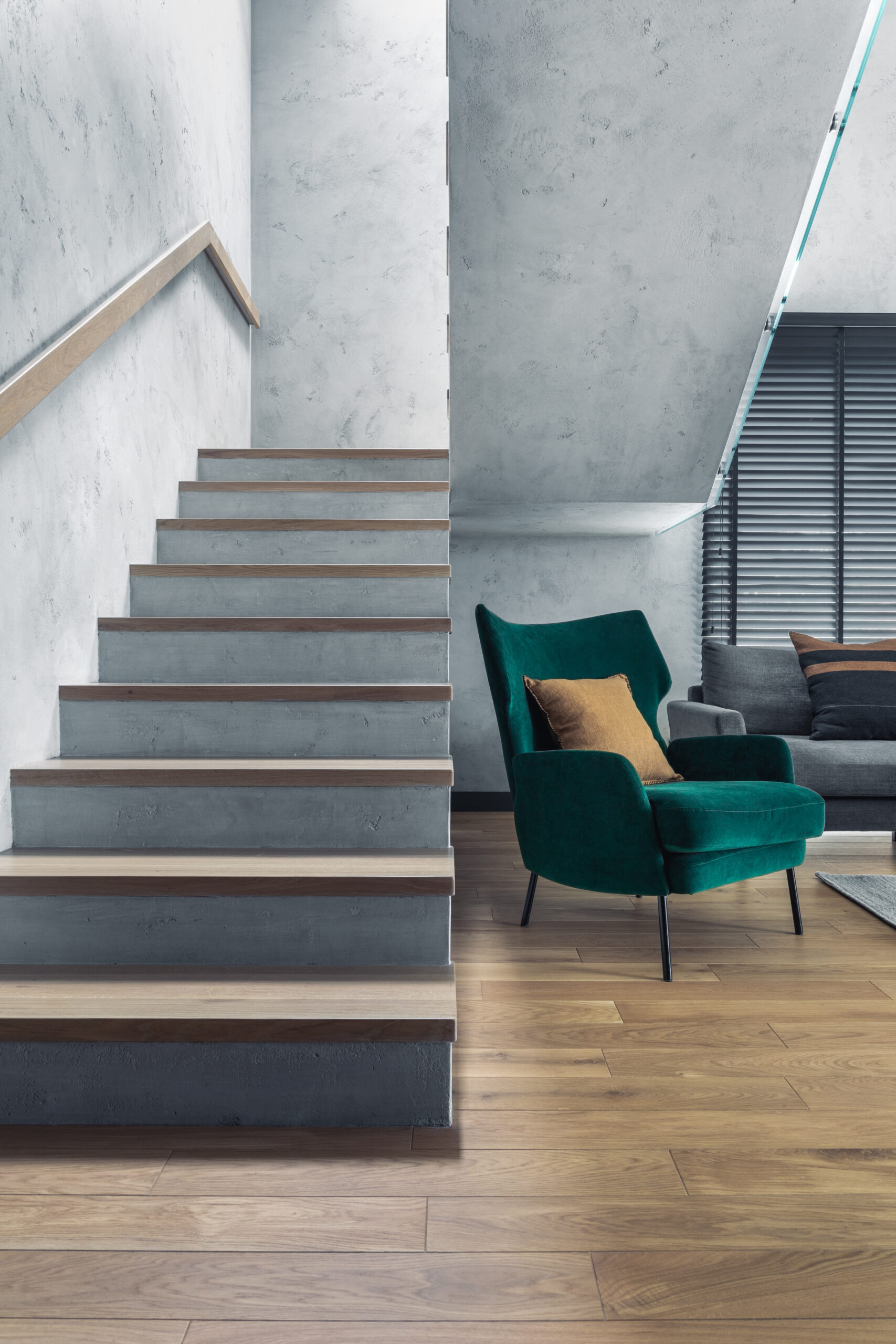 Eine Treppe aus Beton und Holz neben einem blaugrünen Sessel im Wohnzimmer.