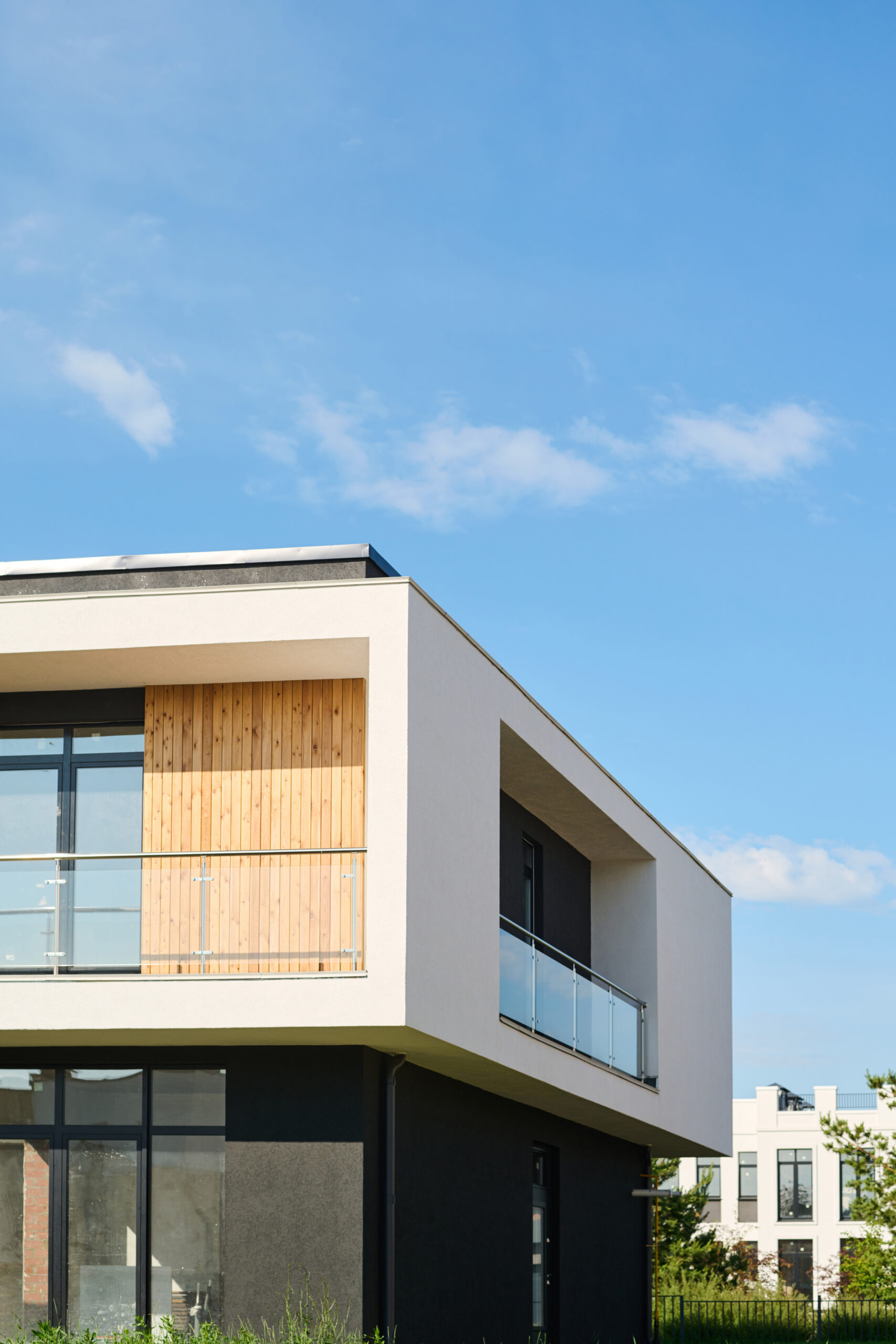 Modernes zweistöckiges Gebäude mit Flachdach, holzverkleidetem Balkon und Glasgeländern vor blauem Himmel.