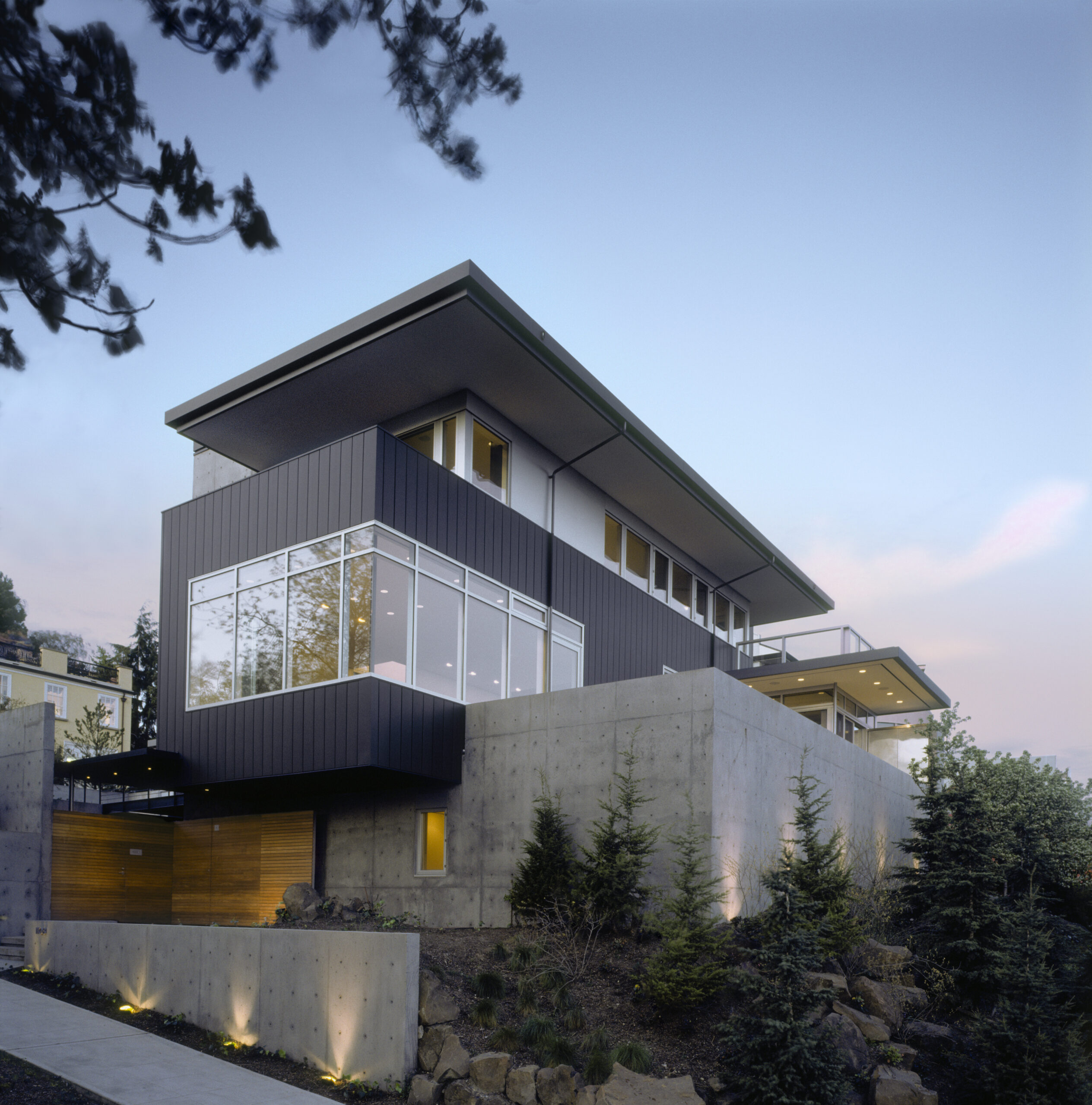 Ein modernes Haus mit schwarzer vertikaler Fassadenverkleidung und großen Fenstern, das auf einem Betonsockel errichtet wurde.