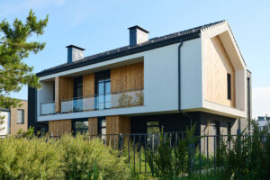 Ein modernes zweistöckiges Haus mit weißen und dunkelgrauen Außenwänden, Akzenten aus Holzvertäfelungen und einem Balkon im zweiten Stock mit Glasgeländer.