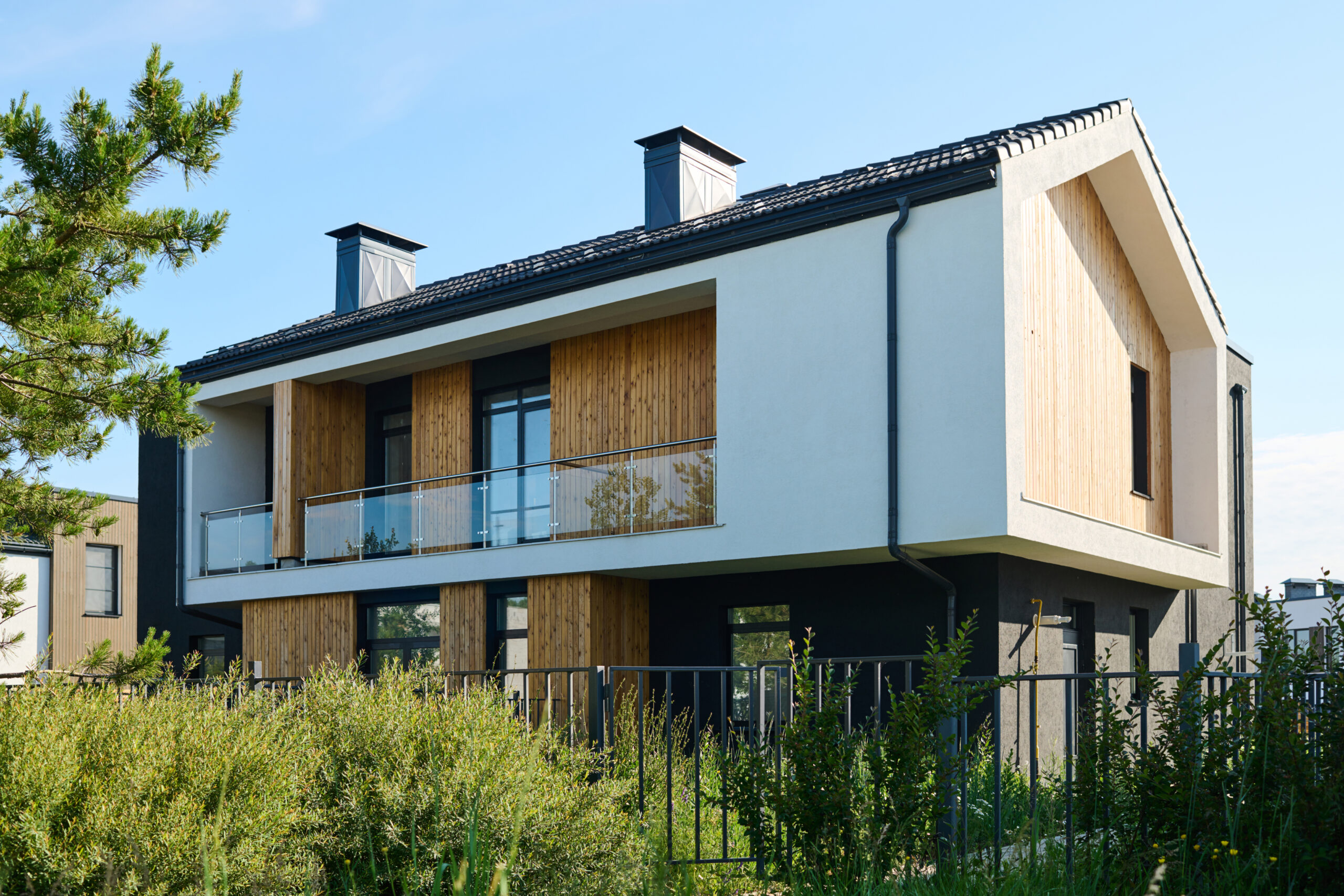 Ein modernes zweistöckiges Haus mit weißen und dunkelgrauen Außenwänden, Akzenten aus Holzvertäfelungen und einem Balkon im zweiten Stock mit Glasgeländer.