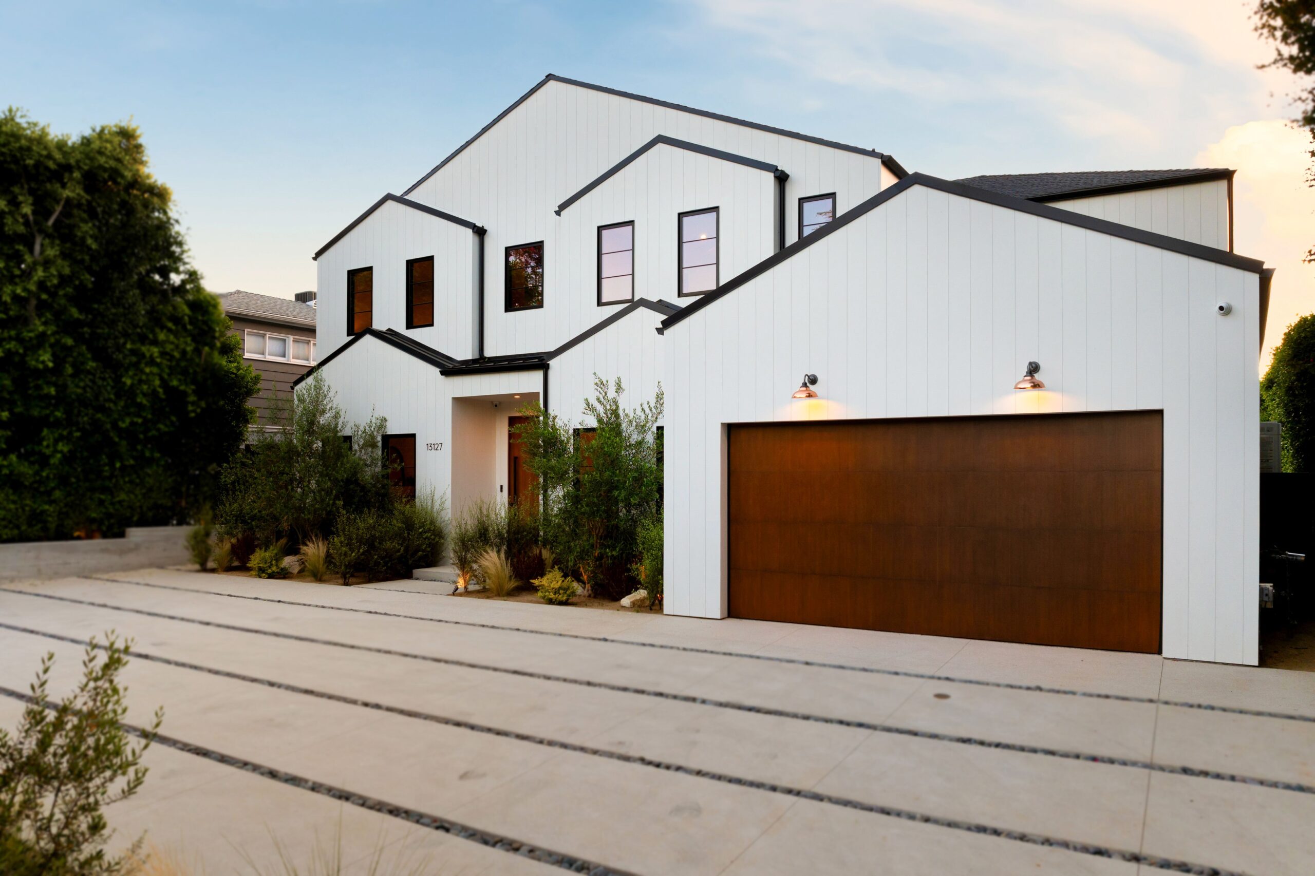 Ein zweistöckiges, weißes, modernes Bauernhaus mit schwarzen Zierleisten, einem großen braunen Garagentor und einer Betonauffahrt.